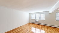 Located at 46 Jerseyville Ave in Freehold, NJ, this well-appointed one-bedroom, one-bathroom unit offers a thoughtfully designed single-floor layout with consistent hardwood flooring throughout. The living room is bright and airy, featuring large multi-pane windows that flood the space with natural light, crown molding, a baseboard heating system, and a wall-unit air conditioner for year-round comfort. The kitchen-living area is efficiently designed with white shaker-style cabinetry, stainless steel appliances including a refrigerator and dishwasher, a classic subway tile backsplash, and durable wood-tone flooring. The generously sized bedroom is a standout feature, offering dual built-in closets with shelving for ample storage, crown molding, a window with natural light, and its own wall-unit air conditioner. An additional hallway area provides extra built-in shelving, enhancing storage options throughout. The bathroom is clean and modern, appointed with a tub-shower combination enclosed by a sleek sliding glass door, white tile surround, and a window for natural ventilation. The unit's consistent white walls and warm hardwood floors create a bright, cohesive aesthetic throughout.
