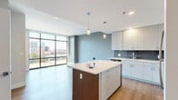 Located at 601 Bond Ave in Grand Rapids, MI, this modern one-bedroom, one-bathroom unit offers a thoughtfully designed open-concept layout with clean, contemporary finishes. The kitchen is a standout feature, boasting a large center island with a quartz countertop, sleek white and light-wood cabinetry, a blue-gray tile backsplash, and a full suite of stainless steel appliances including a range, microwave, dishwasher, and refrigerator. Pendant lighting illuminates the island, while floor-to-ceiling windows flood the living area with natural light and offer views of the surrounding Grand Rapids cityscape. Wood-look flooring runs throughout the unit, adding warmth and continuity. The bedroom is a comfortable, well-proportioned room featuring neutral walls, wood-look flooring, and a window with urban views, with a dedicated closet nearby. The bathroom is finished with a vibrant teal vanity, white quartz countertop, large-format tile in the shower/tub surround, and wood-look flooring, creating a lively yet clean aesthetic. The overall ambiance is bright, modern, and urban, making this a well-appointed home in the heart of Grand Rapids.
