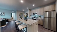 Located at 40000 Argento Way in Kannapolis, NC, this well-appointed single-floor residence offers a thoughtfully designed open-concept layout with modern finishes throughout. The kitchen serves as a central hub of the home, showcasing a large granite-topped island with bar seating, light wood cabinetry extending to the ceiling, a subway tile backsplash, and a full suite of stainless steel appliances. Wood-style flooring runs throughout the main living areas, complementing the neutral gray tones of the walls and creating a cohesive, contemporary aesthetic. The living area is generously proportioned, filled with natural light and offering a warm, inviting ambiance. Multiple bedrooms provide comfortable retreats, each featuring plush carpeting, large windows with ample natural light, and walk-in closets for storage. The primary bedroom includes a ceiling fan and direct access to a private en-suite bathroom. The bathrooms are finished with granite countertops, undermount sinks, wood-toned vanities, and wood-style flooring, maintaining the refined design language found throughout the home. An in-unit laundry area adds everyday convenience. Overall, the space balances modern style with functional living in a clean, neutral palette ideal for a variety of lifestyles.