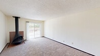 Located at 3403 Jersey Ridge Rd in Davenport, Iowa, this single-floor residence offers three bedrooms and two bathrooms within a well-organized, efficiently laid-out floor plan. The living area features plush carpeting, a striking freestanding wood-burning stove as a central focal point, and a sliding glass patio door that fills the room with natural light and provides outdoor views. Textured ceilings are present throughout the home. A wood-floored hallway connects the living area to the rest of the unit, leading to the kitchen and bedrooms. The galley-style kitchen is equipped with warm oak cabinetry, ample counter space with laminate surfaces, a double sink, and white appliances including a refrigerator and range, with a ceiling fan adding comfort to a nearby dining area. Each of the three carpeted bedrooms offers a window with outdoor views, with the primary bedroom featuring a closet and direct access to a bathroom. The two bathrooms include a combination tub/shower unit and a separate walk-in shower stall, each with oak vanities and bright overhead lighting. Dark wood trim and doors provide a consistent design accent throughout the home.