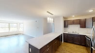 Located at 375 Autumn Pond Way in Essex Junction, Vermont, this two-bedroom, two-bathroom single-floor home offers a well-organized layout designed for comfortable everyday living. The open-concept kitchen and living area serves as the heart of the home, featuring rich dark-stained shaker-style cabinetry, light countertops, stainless steel appliances including a refrigerator and range, a double-basin sink, and a central island illuminated by pendant lighting. The living area extends naturally from the kitchen, showcasing durable hardwood-style flooring and a generous bank of windows that flood the space with natural light and offer views of the surrounding neighborhood. Both bedrooms are carpeted and finished with neutral tones, providing a calm and restful atmosphere. Each room features a window with outdoor views and baseboard heating. The two bathrooms are clean and functional, with tile flooring, dark wood vanities with light countertops, and tub/shower combinations. One bathroom also features an accessibility grab bar. A dedicated closet provides additional storage. The overall aesthetic is clean, modern, and move-in ready, with a consistent neutral palette throughout that makes the space feel bright and welcoming.