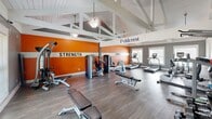 The Fieldcrest Fitness Center at 31 Trillium Cir in Dothan, Alabama is a well-appointed, single-room exercise facility designed to support a comprehensive workout experience. The space is defined by its striking vaulted ceiling with exposed white structural beams, which lend an open, airy feel and generous vertical height throughout. Hardwood-style flooring runs across the entire room, providing a clean and durable surface for all fitness activities.

The interior is boldly divided into two functional zones, clearly identified by large wall signage: a Strength area and a Cardio area. The accent walls are painted a vivid orange with white horizontal striping, creating an energizing atmosphere. The Strength zone is equipped with a cable machine, weight bench, dumbbell rack with a full range of free weights, medicine balls, resistance equipment, and a multi-functional cable tower. The Cardio zone features treadmills, elliptical trainers, a stationary bike, and a stair climber.

Natural light enters through multiple windows, offering views of the surrounding community and keeping the space bright and welcoming. Ceiling fans with integrated light fixtures provide additional ventilation and illumination. The overall design balances motivating aesthetics with practical functionality, making this fitness center a well-equipped destination for residents seeking a convenient and effective place to exercise.