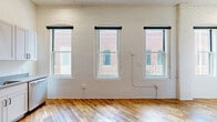 Located at 219 N Columbus St in Lancaster, OH, this one-bedroom, one-bathroom unit delivers a compelling blend of historic character and modern updates. The open-plan living and kitchen area is anchored by warm, natural hardwood floors and striking white-painted exposed brick walls that lend an authentic industrial-loft aesthetic. Soaring ceilings with exposed ductwork amplify the sense of openness and light, while tall arched windows frame views of the surrounding downtown streetscape, flooding the space with natural light throughout the day. A bold teal entry door adds a distinctive pop of color upon arrival. The kitchen is well-appointed with white shaker cabinetry, sleek countertops, and a full suite of stainless steel appliances including a refrigerator with ice maker, range, microwave, and dishwasher. The bedroom features the same warm hardwood flooring, high ceilings, and a sliding closet door, creating a comfortable and airy retreat. The bathroom is finished with classic white subway tile in a walk-in shower enclosed by sliding glass doors with dark-framed hardware, complemented by mosaic tile flooring and clean white walls. Throughout the unit, the combination of preserved architectural elements and contemporary finishes creates a refined, urban living environment.