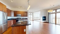 Located at 3115 Lilly Rd in Brookfield, WI, this well-appointed single-floor residence offers four bedrooms, three bathrooms, and a thoughtfully designed open-concept layout. The combined kitchen, dining, and living area forms the heart of the home, showcasing rich hardwood flooring, warm cherry wood cabinetry, dark granite countertops, stainless steel appliances, and a central island with a built-in sink. A pendant light fixture and track lighting add a modern touch, while large windows and sliding doors lead to two balconies, filling the space with natural light. The living area features a sleek built-in fireplace set against a crisp white wall, complemented by plush carpeting. The spacious primary bedroom is bathed in natural light from an expansive bank of windows with scenic outdoor views, and is complemented by a well-organized walk-in closet with built-in wire shelving. The en-suite bathroom includes both a soaking tub and a glass-enclosed shower, framed by wide windows. Additional bedrooms offer comfortable carpet flooring and ceiling fans. Five closets throughout the home provide ample storage, and a utility room adds further practicality to this clean, modern Brookfield residence.