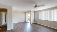 This single-floor residence offers a thoughtfully designed layout with a blend of hard-surface and carpeted flooring throughout. The main living area is bright and open, featuring durable wood-style flooring, crown molding, a ceiling fan, and vertical blinds that filter natural light. Sliding doors connect the living space to an outdoor balcony, extending the sense of openness.

The kitchen is efficiently arranged with light wood cabinetry, white appliances including a refrigerator, electric range, and microwave, as well as a peninsula with a built-in sink and countertop overhang ideal for casual dining. The kitchen opens directly to the main living and dining areas, supporting an open-concept flow.

The bedrooms are carpeted for comfort and each features a ceiling fan with light fixture and access to natural light via vertical-blind-covered windows or sliding doors. The primary bedroom includes a spacious walk-in closet outfitted with wire shelving and built-in hanging rods. The bathroom is clean and functional, offering a wide vanity with ample under-sink storage and a well-lit mirror.

A dedicated laundry area houses a full-size washer and dryer with overhead shelving for added storage. The space is finished with consistent neutral tones, white trim, and recessed lighting throughout, creating a cohesive and practical living environment.