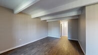 Located at 6900 E Evans Ave in Denver, Colorado, this one-bedroom, one-bathroom residence offers a well-organized single-floor layout across a comfortable and functional footprint. The living room greets you with distinctive exposed beam ceilings, neutral-toned walls, and rich dark hardwood-style flooring that extends throughout the main living areas, creating a warm yet modern aesthetic. Natural light enters through vertical-blind-covered windows and a glass-paneled entry door, enhancing the open feel of the space. The galley-style kitchen is efficiently designed with ample white cabinetry on both sides, stone-patterned countertops, a stainless steel sink with a modern faucet, and white appliances including a range and refrigerator, all set atop light wood-look flooring. A hallway connects the main living area to the private spaces, including a generously sized primary bedroom finished with plush carpet, exposed beam ceiling detail, a large window with vertical blinds, baseboard heating, and a built-in sliding-door closet with shelving. The bathroom features wood-look flooring, a full tub-shower combination with white tile surround, and clean white fixtures. This residence provides a practical and comfortable living environment in a well-connected Denver neighborhood.