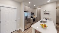 This thoughtfully laid-out single-floor residence offers a seamless blend of modern design and comfortable living. The open-concept kitchen flows directly into the living area, creating an inviting, connected space ideal for everyday living. The kitchen is equipped with stainless steel appliances, including a French door refrigerator, built-in microwave, and range, all complemented by contemporary light wood cabinetry and a white quartz island with an undermount sink. Recessed lighting throughout enhances the bright, clean aesthetic.

The living area features wood-look flooring, a ceiling fan, and generous natural light from large windows with blinds. A dedicated dining nook accommodates a round wooden table beneath a stylish pendant light. A built-in fireplace adds a warm focal point to the main living space.

The two bedrooms are comfortably sized, each featuring ceiling fans, wood-look flooring, and closet storage. A barn-style sliding door adds a distinctive design detail to one bedroom. The unit includes two full bathrooms — one with a tiled tub-shower combination and another with a glass-enclosed walk-in shower — both finished with modern vanities and cabinetry. An in-unit laundry area rounds out this well-appointed residence.