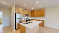 This single-floor residence offers a thoughtfully designed layout that maximizes functionality and comfort. The open-concept kitchen and living room form the heart of the home, featuring light hardwood-style flooring and warm neutral tones throughout. The kitchen is well-equipped with honey-toned wood cabinetry extending to the ceiling for ample storage, crisp white countertops, stainless steel appliances including a refrigerator, range, and over-the-range microwave, and a central island with a double-basin sink and a modern pull-down faucet — ideal for both cooking and casual dining. The adjoining living area is bright and airy, highlighted by a ceiling fan and large sliding glass doors that open to a private balcony with outdoor views of surrounding greenery. The bedroom offers plush carpeting, soft neutral walls, and a built-in sliding-door closet with integrated shelving for organized storage. The bathroom features a clean, modern vanity with a white countertop, undermount sink, wood cabinetry with brushed nickel hardware, a large mirror, and a separate shower. The consistent use of light wood tones, white trim, and recessed lighting throughout creates a cohesive and welcoming ambiance.