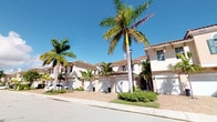 This single-floor Mediterranean-style residence makes a striking first impression with its well-appointed exterior design. The facade showcases classic stucco finished walls in warm, neutral tones, complemented by a distinctive terra cotta barrel tile roof — hallmarks of the Mediterranean architectural style commonly found in South Florida communities. Tall, swaying palm trees and carefully maintained tropical greenery frame the property, enhancing its curb appeal and evoking a relaxed, resort-like atmosphere. A paver driveway leads to an attached garage, adding both convenience and visual appeal to the approach. The exterior benefits from abundant natural Florida sunlight, which highlights the architectural detailing and the rich, warm palette of the building's finishes. Wall-mounted coach lighting adds a refined touch to the entryway, contributing to the overall elegance of the home. The surrounding landscape features manicured shrubs and tropical plantings that provide color and texture throughout the year. The architecture reflects a cohesive community aesthetic, with neighboring units sharing similar design elements, creating a harmonious and visually appealing streetscape. Overall, this property embodies the relaxed yet refined character of Florida living.