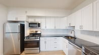 This single-floor residence is designed with a clean, contemporary aesthetic throughout. The kitchen is well-appointed with white shaker-style cabinetry, dark countertops, a subway tile backsplash, and a full suite of stainless steel appliances including a gas range, built-in microwave, refrigerator, and dishwasher. A pass-through counter connects the kitchen to the main living area, enhancing the open feel of the layout.

The expansive living area is anchored by light hardwood-style flooring that extends throughout the unit, contributing to a bright and cohesive atmosphere. Large sliding glass doors span a generous portion of the living space, flooding the interior with natural light and providing direct access to a private balcony that overlooks a lush, tree-lined landscape.

The bedrooms are well-sized with clean white walls and the same warm flooring. One room includes access to a generously proportioned walk-in closet with built-in shelving and hanging rods. Two bathrooms serve the unit—one featuring a full tub/shower combination, and another with white cabinetry, a dark countertop vanity, and accessible grab bars. The overall design is bright, functional, and move-in ready.