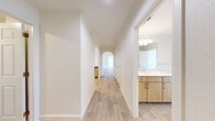 This well-appointed single-story residence at 2002 Battlecreek Dr offers a clean, modern aesthetic with light wood-style flooring flowing throughout the main living areas and neutral tones that create a bright, open atmosphere. The living room serves as the heart of the home, featuring a tiled fireplace with a white mantel, a ceiling fan with integrated lighting, and sliding glass doors that open onto a private patio, allowing natural light to fill the space. Adjacent to the living room, the dining area connects seamlessly to the kitchen, which is equipped with light wood cabinetry, quartz countertops, stainless steel appliances including a range and over-the-range microwave, and a deep single-basin sink with a gooseneck faucet. The hallway, accented by a charming arched doorway, leads to three generously sized bedrooms, each outfitted with plush carpeting and ceiling fans. The primary bedroom features a dedicated closet and direct access to a well-designed en-suite bathroom boasting a dual-sink vanity with quartz countertops, warm wood cabinetry, a soaking tub, and a separate shower. The second bathroom mirrors the same modern finishes with a single-sink vanity and wall-mounted storage cabinet. A dedicated laundry room houses a full-size washer and dryer. Five closets throughout provide ample storage.