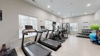 Located at 5813 Lilliana Ln in Whitestown, Indiana, this fitness center offers a thoughtfully designed workout environment with a clean, modern aesthetic. The single-floor space features light hardwood-style flooring, neutral-toned walls, and recessed lighting complemented by a ceiling fan, creating a comfortable and well-lit atmosphere throughout.

Large windows with slatted blinds line the walls, allowing ample natural light to filter in while providing views of the surrounding exterior. Multiple wall-mounted flat-screen televisions are positioned throughout the room, offering entertainment during workouts.

The cardio zone is well-appointed with treadmills, elliptical trainers, a stationary bike, and a water rowing machine, all arranged to maximize usable floor space. A multi-functional cable and weight machine anchors the strength training area, accompanied by an adjustable weight bench. A dedicated free weight section includes a full rack of dumbbells in graduated sizes. Functional training accessories such as stability balls, medicine balls, and foam rollers are neatly organized on a storage rack. A large floor-to-ceiling mirror along one wall enhances the sense of space and allows users to monitor their form. The overall layout is efficient and accessible, making this fitness center a versatile facility suited for a wide range of workout routines.