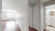 Located at 905 Burnside Ave in East Hartford, Connecticut, this single-floor unit offers a clean, neutral aesthetic with a thoughtfully laid-out interior. Rich hardwood flooring runs throughout the main living areas and bedrooms, providing warmth and continuity across the space.

The open living and dining area is generously proportioned, bathed in natural light from large windows and accented by an elegant chandelier overhead. A wall-mounted AC unit and baseboard heating ensure year-round comfort. The kitchen is accessible via a half-wall pass-through and is well-appointed with white cabinetry, dark granite countertops, a classic subway tile backsplash, and stainless steel appliances including a range, microwave, and refrigerator.

The bedrooms feature the same hardwood flooring, neutral gray walls, and natural light from windows fitted with blinds. One bedroom includes a spacious closet with built-in shelving and hanging rods, offering practical storage. A hallway connects the main rooms, with interior doors providing clear separation between living and private spaces.

The bathroom is finished with light tile flooring, white wainscoting, a vanity with under-cabinet storage, a medicine cabinet mirror, and a bathtub/shower combination, delivering a clean and functional design. Overall, the space presents a move-in ready interior with consistent finishes throughout.
