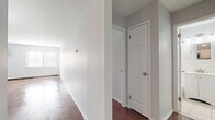 Located at 905 Burnside Ave in East Hartford, Connecticut, this single-floor unit offers a clean, neutral aesthetic with a thoughtfully laid-out interior. Rich hardwood flooring runs throughout the main living areas and bedrooms, providing warmth and continuity across the space.

The open living and dining area is generously proportioned, bathed in natural light from large windows and accented by an elegant chandelier overhead. A wall-mounted AC unit and baseboard heating ensure year-round comfort. The kitchen is accessible via a half-wall pass-through and is well-appointed with white cabinetry, dark granite countertops, a classic subway tile backsplash, and stainless steel appliances including a range, microwave, and refrigerator.

The bedrooms feature the same hardwood flooring, neutral gray walls, and natural light from windows fitted with blinds. One bedroom includes a spacious closet with built-in shelving and hanging rods, offering practical storage. A hallway connects the main rooms, with interior doors providing clear separation between living and private spaces.

The bathroom is finished with light tile flooring, white wainscoting, a vanity with under-cabinet storage, a medicine cabinet mirror, and a bathtub/shower combination, delivering a clean and functional design. Overall, the space presents a move-in ready interior with consistent finishes throughout.