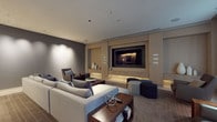 This refined single-floor space showcases a seamless blend of contemporary design and understated luxury. The main living area is anchored by a striking built-in media wall clad in light wood cabinetry, housing a large flat-screen display with under-cabinet accent lighting that adds warmth and depth to the room. Recessed ceiling lighting throughout provides a layered illumination scheme, complementing the cool-toned recessed spots that cast elegant washes of light across the muted grey walls.

Generous seating is thoughtfully arranged to encourage both entertainment and relaxed conversation, featuring a large sectional sofa in neutral upholstery, a leather lounge chair, a swivel accent chair, and a collection of modular ottomans. A dark wood coffee table serves as a grounding centerpiece, styled with curated decorative objects. The flooring transitions between rich wood and a patterned tile, adding visual texture throughout the space.

Natural light enters through tall windows dressed with sheer patterned curtains, offering views of lush greenery beyond. A frosted glass sliding door leads to an adjacent area, maintaining privacy while preserving the open, airy feel. Built-in shelving niches display minimalist ceramic vessels, reinforcing the space's calm, gallery-like ambiance. Smart home control panels are discreetly integrated into the walls, reflecting the space's commitment to modern convenience and polished design.