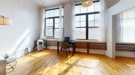 Located at 179 St Paul St in the heart of Rochester, NY, this loft-style unit offers an open, single-floor layout with a distinct urban character. Warm hardwood floors run throughout the entire space, complementing the painted exposed brick walls that lend an industrial aesthetic. The open-plan kitchen and living area form the core of the unit. The kitchen is equipped with white cabinetry, a stainless steel countertop workspace, a coil-top range, and a sink, with a notable large metal-paneled accent wall and a sliding barn door that adds a rustic-industrial touch. An embossed tin ceiling overhead further enhances the vintage character of the kitchen area. The living area is generously proportioned, with tall windows allowing abundant natural light to pour in, illuminating the hardwood floors and white brick walls. A dedicated closet provides convenient storage. The bathroom continues the hardwood flooring and features white tiled walls, a standalone glass-enclosed shower stall, and a clean, functional layout. The overall ambiance of this space blends historic architectural elements with practical, comfortable living—ideal for those seeking an urban loft experience in downtown Rochester.