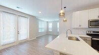 Located at 110 N Chestnut St in Olathe, Kansas, this single-floor residence offers a clean, contemporary design with a thoughtfully laid-out floor plan. The open-concept living and dining area flows seamlessly from the kitchen, bathed in natural light through multiple windows dressed with white blinds. Light-toned hardwood-style flooring runs throughout the main living spaces, adding warmth and continuity to the interior.

The kitchen is a standout feature, equipped with crisp white upper cabinetry, gray lower cabinets, a classic white subway tile backsplash, and stainless steel appliances including a refrigerator, range, and over-the-range microwave. A peninsula with a white quartz countertop and undermount sink is accented by stylish amber glass pendant lights, providing both additional workspace and a casual dining option. French doors in the living area offer access to the exterior, enhancing the sense of openness.

The bedrooms are carpeted in a neutral tone and receive natural light through individual windows. The primary bathroom features a vanity with white quartz countertop, gray cabinetry, a large mirror, and access to a walk-in closet. A second full bathroom includes a tiled tub-shower combination and a matching vanity. Throughout, the neutral color palette and modern finishes create a cohesive and inviting atmosphere.