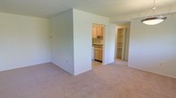 This single-floor unit at 5210 B6 offers a straightforward and functional layout designed for comfortable everyday living. The main living area is finished with wall-to-wall carpet in a neutral tone, creating a warm and inviting atmosphere. Clean white walls throughout lend a bright, open feel to the space.

A partial wall divides the living area from the kitchen, providing a sense of separation while maintaining an open connection between the two spaces. The kitchen features light wood cabinetry, a sink with under-cabinet storage, and tile flooring, offering a practical cooking and prep environment.

Adjacent to the kitchen, a dedicated storage area is fitted with built-in open shelving, ideal for organization and easy access to household essentials. The layout flows efficiently, making good use of the available footprint on a single level.

Overall, the unit presents a clean, move-in-ready environment with a simple, neutral aesthetic that provides a blank canvas for personalization. The combination of carpeted living spaces, a functional kitchen, and integrated storage make this a practical and well-organized space.