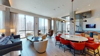 Located in Chicago's vibrant West Loop neighborhood, this upscale amenity floor at Union West delivers a refined blend of contemporary design and versatile functionality. The space is anchored by expansive floor-to-ceiling windows that frame sweeping panoramic views of the Chicago skyline, flooding the interiors with abundant natural light throughout.

The open-plan lounge and dining areas feature light oak hardwood flooring, exposed concrete columns, and warm cove lighting that lend an industrial-chic sophistication to the space. A stylish dining area accommodates a large dark-surfaced table paired with leather safari-style chairs beneath an artistic sculptural pendant light. Adjacent, a relaxed seating area offers plush cream-toned lounge chairs and low tables, ideal for casual gatherings.

A dedicated collaborative zone features a round white table surrounded by bold red chairs under modern pendant lighting, alongside soft lounge seating positioned to take full advantage of the city views. The game room houses a full-size billiards table beneath a multi-globe pendant fixture, complemented by a mounted flat-screen television and direct access to an outdoor terrace.

Flexible, movable white partition walls allow the space to be reconfigured for a variety of event formats. The entry foyer features a dramatic dark tile-clad elevator surround and branded Union West flooring, establishing a polished first impression throughout.