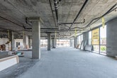 This single-floor commercial shell space presents a rare opportunity to configure a fully customizable office or commercial environment from the ground up. The open floor plate is expansive, supported by structural concrete columns that punctuate the layout while preserving wide, unobstructed spans ideal for flexible planning. Exposed concrete ceilings reveal the raw infrastructure of the building, with visible MEP systems — including electrical conduits, plumbing lines, and HVAC ductwork — already routed overhead and ready for integration into the finished build-out. Polished concrete floors run throughout, providing a clean, neutral base for any design direction. Floor-to-ceiling glazing lines key perimeter walls, flooding the interior with abundant natural light and offering clear sightlines to the surrounding urban environment. Partially framed drywall partitions in select areas indicate that the build-out is actively progressing, with structural rough-ins in place for future rooms and corridors. Emergency exit infrastructure and electrical panels are already installed. The overall character of the space is industrial yet refined, offering a blank canvas with strong bones. Marked as available for office or commercial lease, this space is well-suited for businesses seeking a modern, highly adaptable environment in an urban setting.