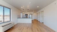 Located at 404 Fountain St in Philadelphia's Manayunk neighborhood, this single-floor unit at The Wright presents a clean, modern aesthetic defined by light hardwood flooring, crisp white walls, and thoughtfully selected finishes. The open-concept layout connects the living area seamlessly to the kitchen, creating a bright, airy feel enhanced by natural light streaming through multiple windows fitted with blinds.

The kitchen serves as a focal point of the space, anchored by a central island with a dark stone countertop, an undermount sink, and white cabinetry with matte black hardware. A classic white subway tile backsplash frames the cooking area, which is equipped with stainless steel appliances including a range, over-the-range microwave, and refrigerator. Pendant lights with an industrial character hang above the island, adding warmth to the space.

The living area is generously proportioned, bathed in natural light from large windows, and features a wall-mounted HVAC unit for year-round climate control. Additional rooms offer similarly light-filled, versatile spaces with the same consistent hardwood flooring.

The bathroom is finished with wood-look tile flooring, a white vanity, and a tub-shower combination clad in marble-style tile, lending an elevated, spa-like quality to the space.