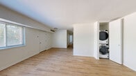 This single-floor unit offers a clean, modern aesthetic with light wood-style flooring that runs throughout the entire space, complemented by crisp white walls and bright, open interiors. The front entry leads into a spacious living area featuring a well-proportioned layout with a dedicated closet and convenient in-unit stacked washer and dryer tucked neatly into an alcove, adding to the home's functional appeal.

The kitchen is thoughtfully designed with white shaker-style cabinetry accented by matte black hardware, sleek quartz countertops with subtle marble veining, and a dishwasher — providing both style and practicality. A hallway connects the living areas to the private quarters of the unit.

The bedrooms are generously sized, each featuring light-filled windows with views of surrounding greenery, creating a calm and inviting atmosphere. One bedroom includes a built-in closet with shelving and a hanging rod, offering ample storage. The bathroom is finished with white subway tile surrounding a full bathtub and shower, complemented by matte black fixtures for a contemporary touch, along with a white vanity and wood-tone flooring that ties the space together cohesively.
