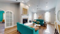 This thoughtfully designed single-story space offers a dynamic blend of architectural character and bold, contemporary styling. The main living area immediately impresses with soaring vaulted ceilings, a ceiling fan, and recessed lighting that illuminate rich hardwood flooring throughout. A striking white fireplace serves as the room's focal point, flanked by vibrant teal sofas and accented by geometric gold wall art above the mantle. Natural light streams in through multiple windows dressed in sheer curtains, enhancing the bright, airy atmosphere.

The open-concept kitchen features white cabinetry, dark countertops, and a peninsula with bar seating, flowing seamlessly into the living space. A dedicated office area includes a built-in desk workspace, plush carpeting, crown molding, and a decorative chandelier, with an adjacent sitting nook furnished in teal patterned chairs.

A separate lounge or flex room boasts a bold teal accent wall, vaulted ceiling, and yellow leather seating around a dark round table, offering a vibrant gathering space. Throughout, arched doorways and French doors add architectural elegance, while a cohesive teal, gold, and neutral palette ties each area together into a lively, well-curated environment.