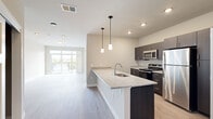 This well-appointed single-floor residence showcases a thoughtfully designed open-concept layout that seamlessly connects the kitchen and living area. The kitchen is a standout feature, centered around a generous granite-topped island with an undermount sink and elegant pendant lighting. Dark espresso cabinetry contrasts beautifully with the light granite countertops, while stainless steel appliances — including a refrigerator, microwave, and electric range — complete the space with a polished, modern aesthetic. Light wood-tone flooring flows throughout the main living areas, contributing to a bright and airy feel.

The living area is bathed in natural light, thanks to a full-width sliding glass door that opens onto a private balcony with a railed deck and views of the surrounding greenery and skyline. The bedrooms are carpeted for comfort and feature neutral tones, with access to well-sized walk-in closets equipped with wire shelving systems for organized storage. The bathroom continues the home's design language with matching dark cabinetry, granite countertops, an undermount sink, and a framed mirror. Throughout the space, clean lines, neutral color palettes, and consistent finishes create a cohesive, contemporary living environment.