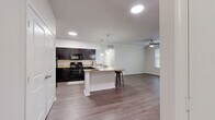 This single-floor residence is designed with an open-concept layout that seamlessly connects the kitchen and living areas, creating a spacious and cohesive environment. The kitchen is well-equipped with dark espresso cabinetry, granite-style countertops, and a full suite of black appliances, including a range, microwave, and refrigerator. A central island with pendant lighting above provides additional prep space and casual seating, while recessed lighting ensures the area is well-lit throughout.

The living area extends naturally from the kitchen, featuring crown molding, a ceiling fan, and access to an exterior door flanked by windows that invite natural light. Wood-style flooring runs consistently throughout the home, lending a cohesive and contemporary aesthetic to each room.

The bedrooms are well-proportioned, each featuring ceiling fans, multiple windows with blinds, and the same durable wood-style flooring. The primary bedroom connects to a spacious bathroom with a dual-sink vanity topped with granite-style counters, dark cabinetry, and a soaking tub. An adjoining walk-in closet offers extensive wire shelving and hanging space. A secondary bathroom mirrors the design with a single-sink vanity and tub-shower combination.