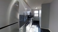 This single-floor space showcases a thoughtfully designed galley-style kitchen with a contemporary aesthetic. The kitchen features floor-to-ceiling high-gloss white cabinetry that maximizes vertical storage, complemented by dark granite or stone countertops that create a striking contrast. A textured mosaic tile backsplash in dark tones adds visual depth and a modern edge to the space.

Stainless steel appliances, including a full-size Frigidaire refrigerator, a range, a microwave, and a dishwasher, are seamlessly integrated throughout. The deep single-basin undermount sink is paired with a sleek black faucet, maintaining the cohesive color palette. Dark, large-format floor tiles run the length of the kitchen, contributing to the polished, uniform look.

Natural light enters through a double-hung window at the far end of the kitchen, providing ventilation and a glimpse of the surrounding cityscape. Recessed flush-mount ceiling fixtures provide consistent overhead lighting. The overall ambiance is clean, functional, and modern, with a deliberate monochromatic contrast between the dark surfaces and the bright white cabinetry.