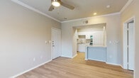 This thoughtfully designed single-story residence offers a functional and cohesive layout across six distinct spaces. The living room serves as the heart of the home, featuring light hardwood-style flooring, crown molding, a ceiling fan, and multiple windows that invite abundant natural light and outdoor views. A glass-panel door provides direct exterior access, enhancing the airy feel of the space.

The kitchen connects seamlessly to the living area via a peninsula counter with a raised breakfast bar, making it ideal for casual dining or entertaining. White cabinetry, stainless steel appliances including a range and microwave, a stainless sink, and light countertops give the kitchen a clean, contemporary look. An adjacent laundry closet with built-in shelving and washer hookups adds everyday convenience.

The bedroom is a comfortably sized retreat with the same warm flooring found throughout, neutral walls, and ample room for furnishings. A dedicated walk-in closet outfitted with wire shelving and hanging rods provides well-organized storage.

The bathroom features a single-sink vanity with cabinetry, a mirrored medicine cabinet, a tiled shower-tub combo, and consistent light flooring that ties the space together. Crown molding and a neutral warm-beige palette unify the home with a clean, welcoming ambiance throughout.