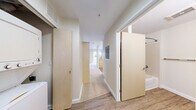 Located at 11030 Main St in Bellevue, WA, this efficiently designed single-floor unit offers a well-organized layout comprising a combined kitchen and living room, a full bathroom, a hallway, and a closet. The living area is finished with soft, neutral-toned carpet and bathed in natural light through large windows and a sliding glass door that opens to a private outdoor space, creating a bright and open atmosphere. The kitchen is outfitted with light maple cabinetry, granite-style laminate countertops, wood-look vinyl flooring, and a full suite of white appliances including a coil-top electric range, dishwasher, and refrigerator — providing all the essentials in a compact, functional footprint. A central hallway connects the main living areas to the bathroom and closet, maintaining a clean and logical flow throughout the space. The bathroom features wood-look vinyl flooring, a light maple vanity with a granite-style countertop and undermount sink, a soaking tub with shower, and a towel bar. Warm, neutral wall tones and light wood accents carry throughout the unit, lending a cohesive and contemporary aesthetic. The closet offers convenient built-in storage, and the overall design maximizes utility within a modest footprint.