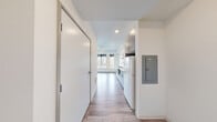 This studio unit at Koz on 420 in Tacoma, Washington, offers a thoughtfully designed single-floor layout that maximizes every square foot of its compact footprint. The space features a clean, modern aesthetic throughout, with light wood-look flooring and crisp white walls that create a bright, airy feel.

The galley-style kitchen is efficiently appointed with two-tone gray and white cabinetry, ample upper and lower storage, a double-basin stainless steel sink, a built-in cooktop, microwave, and a full-size refrigerator — all within easy reach in a streamlined configuration. Recessed lighting illuminates the kitchen and hallway areas.

The main living area benefits from a ceiling fan and a pair of large windows fitted with black roller shades, framing views of the surrounding Tacoma neighborhood and mature trees. The windows draw in generous natural light, enhancing the open feel of the space.

The bathroom is finished in a clean, minimalist style with wood-look tile flooring, a floating vanity with a white countertop, a walk-in shower/tub combination, and chrome fixtures. The entry hallway provides a practical transition from the front door into the living space. Overall, this studio presents a functional, modern living environment suited for efficient urban living in Tacoma.