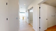 Located at 100 E Second Ave in Longmont, Colorado, this modern 1-bedroom, 2-bathroom unit offers a thoughtfully designed single-floor layout that maximizes every inch of its compact footprint. The open-concept living and kitchen area is anchored by light-toned hardwood flooring, crisp white walls, and abundant natural light streaming through a large sliding glass door that leads to a private balcony with expansive outdoor views. The kitchen is well-appointed with stainless steel appliances — including a French door refrigerator, electric range, and over-the-range microwave — complemented by granite countertops, a tile backsplash, and a mix of white upper cabinetry and natural wood lower cabinets. A freestanding island with a granite top adds additional prep and casual dining space. The living area is open and bright, offering a clean, versatile canvas. The bedroom features plush wall-to-wall carpeting, a ceiling fan, and a sliding closet. A stylish barn door accents the hallway, adding a contemporary design touch. Two closets and an in-unit laundry area provide practical storage solutions, rounding out this well-equipped and modern Longmont residence.