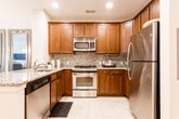 Located at 140 Mayhill St in Saddle Brook, NJ, this single-floor residence offers a thoughtfully designed open-concept layout that seamlessly connects the kitchen, dining, and living areas. The kitchen is a standout feature, equipped with rich dark-wood cabinetry, granite countertops, a mosaic tile backsplash, and a full suite of stainless steel appliances including a gas range, microwave, dishwasher, and refrigerator. A peninsula with an undermount sink provides additional prep space and serves as a natural divider between the kitchen and the adjacent dining area. The living room benefits from an abundance of natural light streaming through large windows with classic white blinds and curtain panels, all set over warm hardwood flooring. The bedroom is a comfortable retreat, featuring plush carpeting, multiple windows that invite natural light, and views of an outdoor deck area. The bathroom is well-appointed with warm wood vanity cabinetry, a white countertop, a large mirror, and tile flooring. Throughout the residence, neutral tones and consistent finishes create a cohesive and welcoming ambiance, making this Saddle Brook property a practical and attractive living space.