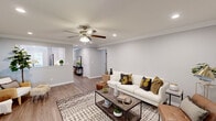This single-floor townhouse at Fairfield Townhouses on Victorian Court in Holtsville, NY, offers a cohesive and modern living experience. The welcoming entryway features crown molding and light hardwood flooring that flows seamlessly throughout the home, setting an elegant tone from the moment you step inside. The spacious living room is anchored by a ceiling fan with integrated lighting, recessed fixtures, and sliding glass doors that open to the outdoors, filling the space with natural light. Crown molding adds a refined architectural detail to the living area. The kitchen is outfitted with crisp white cabinetry, brushed nickel hardware, quartz countertops, a subway tile backsplash, a stainless steel sink, and stainless steel appliances, providing both style and functionality. The bedroom is a serene retreat featuring crown molding, a ceiling fan, hardwood floors, and a window with natural light. Additional rooms provide flexible use, finished with the same clean aesthetic. Two bathrooms serve the home — one featuring a glass-enclosed tub and shower combination with white subway tile and a classic mosaic tile floor, and another with a sleek glass-door shower. The consistent use of neutral tones, crown molding, and hardwood-style flooring throughout creates a unified, modern ambiance.