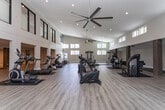 Located at 1373 Lees Chapel Rd in Greensboro, NC, this fitness facility is thoughtfully designed to support a wide range of exercise and wellness activities. The centerpiece of the space is a large, open gymnasium-style workout area distinguished by dramatically high ceilings and an abundance of natural light streaming through rows of clerestory windows positioned along the upper walls. Light wood-look flooring runs throughout, complementing the neutral, warm-toned walls and creating a clean, modern aesthetic. Large ceiling fans provide additional airflow across the expansive workout floor.

The fitness area is well-appointed with a variety of strength and cardio equipment, including cable machines, weight benches, stationary bikes, and exercise balls, all organized to maximize usable floor space. Rustic wood accent columns add a warm, architectural contrast to the otherwise contemporary interior.

Adjacent to the main workout area is a lower-level lounge space with recessed lighting, offering a relaxed setting with seating for rest or recovery. Additional flexible rooms provide storage or multipurpose functionality. A bathroom with a toilet is conveniently accessible from the main floor. The overall layout and design of this facility make it a versatile, professional-grade space suited for personal training, group fitness, or private wellness use.
