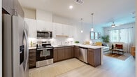Located at 707 W Slaughter Ln in Austin, TX, this one-bedroom, one-bathroom unit offers a thoughtfully designed single-floor layout with modern finishes throughout. The open-concept kitchen and living area serves as the heart of the home, featuring light wood-tone flooring, recessed lighting, and pendant lights over a white quartz kitchen island with bar seating. The kitchen is well-appointed with two-tone cabinetry—white upper cabinets paired with dark wood lower cabinets—a white tile backsplash, and a full suite of stainless steel appliances including a French door refrigerator, range, microwave, and dishwasher. The living area is bright and airy, benefiting from natural light through a window dressed with patterned curtains, and is topped by a ceiling fan. The bedroom is a calm retreat with soft neutral tones, a padded upholstered headboard wall, natural light from a window with blinds, and direct access to a dedicated walk-in closet with built-in shelving and hanging space. The bathroom includes a full soaking tub and shower combo with white tile surround, a dark wood vanity with white countertop, and ample storage cabinetry. Clean lines, a neutral color palette, and consistent wood-tone accents create a cohesive and comfortable living environment throughout.
