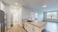 Located at 1330 Nashville Pike in Gallatin, TN, this single-floor, one-bedroom, one-bathroom unit offers a thoughtfully designed layout with modern finishes throughout. Light-toned vinyl plank flooring runs seamlessly across the entire space, lending a clean, cohesive aesthetic.

The open-concept kitchen and living area serves as the heart of the home. The kitchen is equipped with stainless steel appliances — including a range, microwave, and refrigerator — complemented by white shaker-style cabinetry and granite countertops. A peninsula with an integrated sink provides additional prep space and casual seating, making the kitchen both functional and inviting.

The bedroom is a comfortable, well-proportioned retreat featuring a ceiling fan, a large window with views of the surrounding greenery, and a double-door closet for ample storage. The room is filled with natural light, creating a bright and airy atmosphere.

The bathroom features a full tub and shower combination with classic white subway tile surround, a granite-topped vanity with white cabinetry, and recessed lighting, offering a clean and polished finish.

A hallway connects the main living areas to the private spaces. Neutral wall tones throughout the unit enhance the sense of openness and provide a versatile backdrop for a variety of décor styles.