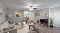This single-floor residence offers a thoughtfully designed layout with consistent wood-look flooring and a neutral gray color palette throughout, creating a cohesive and inviting atmosphere. The open-concept living area serves as the heart of the home, anchored by a classic fireplace with a white mantel and complemented by a ceiling fan overhead. A pass-through window connects the living space to the kitchen, enhancing the sense of openness while maintaining defined areas. The living room flows seamlessly into a dedicated dining area, illuminated by a modern chandelier and framed by a window with a view into the main living space.

The galley-style kitchen is efficiently organized with white cabinetry, light countertops, stainless steel appliances including a range, microwave, and dishwasher, and durable wood-look flooring. The bedroom accommodations are generously proportioned, each featuring ceiling fans and natural light from windows with blinds. The primary bedroom connects to a well-appointed bathroom featuring marble-style countertops, a white vanity, and a separate tub and shower area. An adjacent walk-in closet provides ample storage. The overall design balances functionality with a clean, contemporary aesthetic.