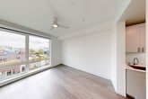Located at 312 W Republican St in Seattle's Queen Anne neighborhood, this efficiently designed one-bedroom, one-bathroom residence offers a clean, modern aesthetic throughout its single floor. The open layout connects the living area and kitchen, maximizing the use of space. Durable wood-look plank flooring runs throughout, complementing the crisp white walls and creating a bright, cohesive interior.

The living area is bathed in natural light through large floor-to-ceiling windows that frame elevated views of the surrounding Seattle cityscape, including glimpses of neighboring rooftops and urban greenery. A ceiling fan with an integrated light fixture adds both function and a contemporary touch to the space.

The kitchen is outfitted with light wood cabinetry, a stainless steel refrigerator, and white countertops, providing a practical and stylish cooking area. The bedroom is a well-proportioned private retreat, featuring a dedicated closet alcove and a smart thermostat panel for climate control.

The bathroom is finished with modern brushed nickel fixtures, a white quartz-topped vanity, and a walk-in shower enclosed by a frosted glass door, offering a clean and functional design. The overall ambiance of the unit is contemporary and minimalist, well-suited for those seeking a low-maintenance urban lifestyle in a prime Seattle location.
