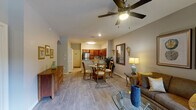 This single-floor residence offers a thoughtfully designed open-concept layout where the living, dining, and kitchen areas flow seamlessly together. The living room is a comfortable and well-lit space featuring light wood-style flooring, a ceiling fan, and large windows that invite natural light and outdoor views of surrounding greenery. Neutral-toned walls complement the warm furnishings, including a plush sofa, patterned accent chair, and a glass-top coffee table. A decorative mirror and wall sconces add character to the space.

The kitchen is efficiently arranged in a U-shape configuration, outfitted with rich cherry wood cabinetry, granite countertops, and a full suite of stainless steel appliances including a refrigerator, range, and built-in microwave. The adjacent dining area comfortably accommodates a round table with seating for four.

Both bedrooms are generously sized, each featuring ceiling fans, wood-style flooring, natural light from well-positioned windows, and access to their own bathrooms. One bedroom includes a walk-in closet. The bathrooms are finished with cherry wood vanities, tile flooring, and tub-shower combinations, each with a window providing natural ventilation.