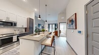 Located in Apollo Beach, FL, this one-bedroom, one-bathroom residence offers a thoughtfully designed open-concept layout with contemporary finishes throughout. Soaring ceilings amplify the sense of space as you enter, with light wood-style flooring extending seamlessly across the main living areas.

The kitchen is a standout, featuring a two-tone cabinetry scheme — crisp white upper cabinets paired with dark wood lower cabinets — complemented by a white tile backsplash, quartz-style countertops, and a full suite of stainless steel appliances. A peninsula island with pendant lighting overhead provides bar seating, making it ideal for casual dining or entertaining.

The open living room benefits from natural light streaming through floor-to-ceiling glass doors, creating a bright and inviting atmosphere. The bedroom features plush carpeting, a large window, and a vibrant accent wall, adding warmth and character to the space.

The bathroom is well-appointed with a teal-toned vanity, ample storage, and a full soaking tub with shower. A dedicated walk-in closet with wire shelving and rod systems provides organized storage. The home also includes a smart home panel, adding a layer of modern convenience to this well-rounded residence.