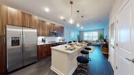 Located at 2020 Morton St in Charlotte, NC, this single-floor residence offers a thoughtfully designed open-concept layout that integrates the living, dining, and kitchen areas into one cohesive space. Dark hardwood-style flooring runs throughout the main living areas, providing a sleek foundation that contrasts with the neutral wall tones and modern finishes.

The kitchen is a standout feature, equipped with rich wood-grain cabinetry extending floor to ceiling, stainless steel appliances including a side-by-side refrigerator, microwave, and range, along with a white quartz countertop island that doubles as a breakfast bar. Stylish glass pendant lights hang overhead, adding an elegant touch. The adjoining living area is generously sized, filled with natural light from large windows, and offers ample room for a full seating arrangement.

Each bedroom features plush carpeting, a ceiling fan, and a bold green accent wall. Both bedrooms connect directly to their own bathrooms, each finished with wood-toned vanities, white quartz counters, tile flooring, and access to a dedicated walk-in closet with built-in shelving, ensuring practical storage throughout.