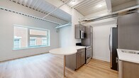 Located in the heart of Lancaster, PA, this thoughtfully designed unit at 101 North Queen Street blends industrial character with modern finishes. The open-concept living and kitchen area anchors the space, showcasing light hardwood flooring, exposed corrugated ceilings with visible ductwork, and structural beams that lend an authentic urban loft aesthetic. The kitchen is well-appointed with gray shaker-style cabinetry, stainless steel appliances including a range and built-in microwave, and a striking rounded white-top island that doubles as a dining or prep surface. A large window frames views of the surrounding brick architecture, filling the living area with natural light. A long, bright hallway with the same light hardwood flooring connects the main living area to the private rooms. The bedroom features soft carpet, an exposed ceiling consistent with the industrial theme, and a dedicated closet with built-in shelving. The full bathroom is finished with a dark wood vanity, white countertop, and neutral tile flooring, with the added convenience of an in-unit washer and dryer nearby. Every detail reflects a clean, contemporary design tailored for comfortable urban living in downtown Lancaster.