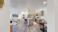 Located at 5555 W Ina Rd in Marana, AZ, this thoughtfully designed 2-bedroom, 2-bathroom residence offers a comfortable single-level layout with a bright, open-concept living space. The kitchen is a standout feature, showcasing light wood cabinetry extending to the ceiling, quartz countertops, stainless steel appliances, a tile backsplash, pendant lighting, and a central island with bar seating — all flowing seamlessly into the dining and living areas. Wood-style flooring runs throughout the main living spaces, lending warmth and continuity. The living room is generously sized, filled with natural light, and opens directly to a private balcony through sliding glass doors, offering outdoor views of the surrounding community. Both bedrooms are carpeted and feature large windows that bring in ample natural light, with dedicated closets providing practical storage. The bathrooms are finished with light wood vanities, quartz countertops, and large mirrors with bright overhead lighting. One bathroom connects directly to a walk-in closet. A dedicated laundry room with shelving adds everyday convenience. The overall aesthetic is clean and contemporary, with a neutral palette that creates a calm, welcoming ambiance throughout.
