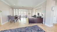 The Gatsby Drive Clubhouse in Montgomery, Alabama offers a thoughtfully designed single-floor community space that blends elegance with functionality. Throughout the interior, large-format travertine tile flooring and crisp crown molding establish a refined architectural tone, while bold navy and white patterned area rugs add a striking visual contrast.

At the heart of the clubhouse is an open reception and leasing area anchored by a substantial dark wood executive desk, providing a professional and welcoming point of entry. Adjacent to this workspace, a spacious lounge area is defined by classical white columns and floor-to-ceiling windows that frame outdoor pool views, flooding the space with natural light.

A dedicated dining area features a round table with upholstered gray chairs and is highlighted by a tile-surround fireplace topped with contemporary artwork, creating a warm and inviting atmosphere. A separate seating alcove with plush armchairs and tall indoor greenery offers a relaxed gathering spot alongside pool-facing windows.

A hallway leads to a well-equipped fitness room, visible through an open doorway and outfitted with cardio equipment. Additional service areas, including a sideboard with a coffee station and tasteful wall art, are conveniently accessible throughout the layout, rounding out this versatile and polished community clubhouse.