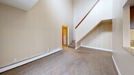 Located at 4380 Wimbledon Dr SW in Grandville, Michigan, this two-story home offers a practical and comfortable layout spread across two floors. The main floor comprises the majority of the living space and includes a generously sized living room distinguished by soaring vaulted ceilings and a staircase with a warm wood handrail, lending an open and airy feel to the space. Baseboard heating units are present throughout, ensuring consistent warmth. The galley-style kitchen is well-appointed with rich wood cabinetry, granite-look countertops, tile flooring, and white appliances including a range and refrigerator, providing ample storage and workspace. A full bathroom on this floor features a clean, white tub-shower surround. Connecting hallways with warm wood-toned doors guide you through the home efficiently. Upstairs, two carpeted bedrooms offer quiet retreats, each finished with neutral walls and window blinds. The primary bedroom includes a built-in closet shelf, while the second bedroom features a window with a view of surrounding greenery and baseboard heating. Soft carpet flooring flows throughout the bedrooms and living areas, complementing the home's warm, neutral color palette and creating a cohesive, inviting atmosphere throughout.