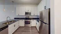 Located at 12310 Moores Lake Rd in Chester, Virginia, this single-floor unit offers a contemporary interior defined by clean lines and consistent, modern finishes. The open-concept layout connects the living area and kitchen seamlessly, with wood-style plank flooring running throughout the space to create visual continuity.

The kitchen is well-appointed with white shaker-style cabinetry featuring black hardware, dark granite countertops, and a full suite of stainless steel appliances including a refrigerator, range, and over-the-range microwave. A peninsula with matching granite provides additional prep space and serves as a natural boundary between the kitchen and living area. Pendant lighting and recessed fixtures illuminate the space effectively.

The living area is open and airy, equipped with a ceiling fan and illuminated by natural light from dual windows fitted with horizontal blinds. The neutral wall tones complement the flooring and contribute to the unit's modern, understated aesthetic.

The bathroom maintains the same design language, featuring a white vanity with dark granite countertop, an undermount sink, a full tub-shower combination with tiled surround, and a grab bar for added accessibility. Overall, the unit presents a cohesive, move-in-ready living environment with quality finishes throughout.