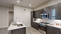 This contemporary single-floor residence showcases a thoughtfully designed open layout with high-quality finishes throughout. The kitchen is a standout feature, equipped with rich dark wood cabinetry, white quartz countertops, a classic subway tile backsplash, and a full suite of stainless steel appliances including a gas range, over-the-range microwave, and a French door refrigerator. A kitchen island with an undermount sink and a sleek pull-down faucet adds both functionality and style, while recessed lighting illuminates the space. Wood-look plank flooring flows through the main living areas, adding warmth and continuity. The bedrooms are finished with plush carpeting and feature large grid-pane windows that invite abundant natural light, complemented by ceiling fans for added comfort. The bathrooms are elegantly appointed with dark wood vanities, white quartz countertops, large framed mirrors, and modern lighting fixtures. The full bath includes a soaking tub and shower combination finished with striking marble-look tile from floor to ceiling. A convenient built-in entryway nook near the front door provides coat hooks and additional cabinetry, offering a practical and organized arrival space. Overall, the residence presents a clean, modern aesthetic with cohesive design elements throughout.